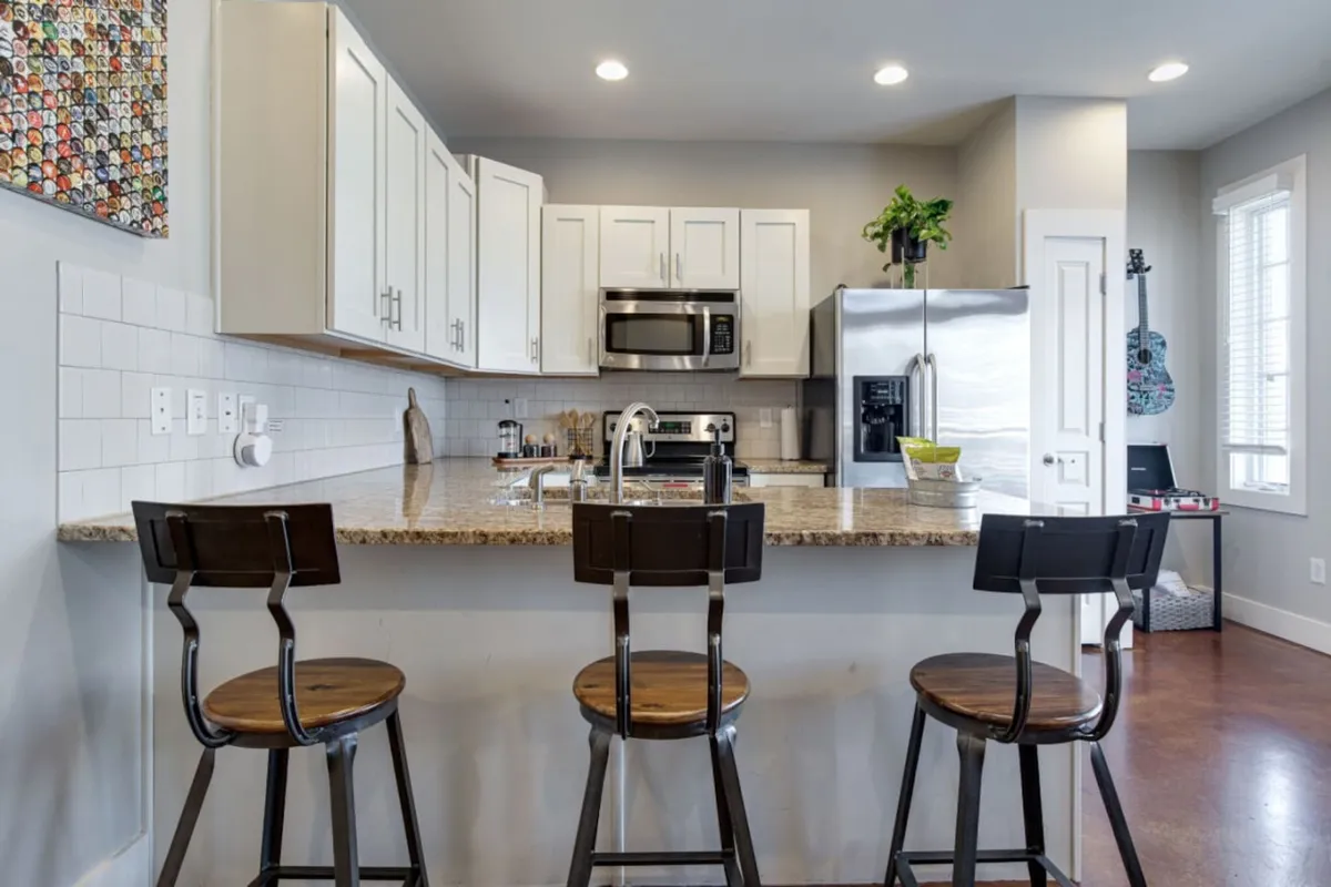 This lively kitchen and dining area features a granite peninsula countertop, sleek stainless steel appliances, bar stools, colorful wall art, and a guitar. The space radiates energy and creativity, offering a setting for socializing, cooking, and casual dining.