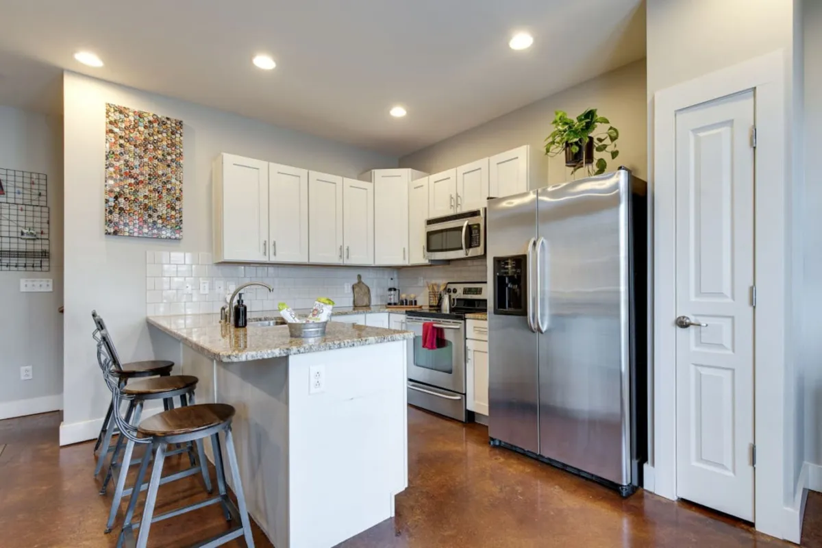 A view of the kitchen area featuring a sleek granite countertop, stainless steel appliances, colorful wall art, and a vibrant potted plant. The space is both modern and homey, set up for shared meals and gatherings, reflecting the kitchen’s role as a hub for family breakfasts and group preparations before outings.