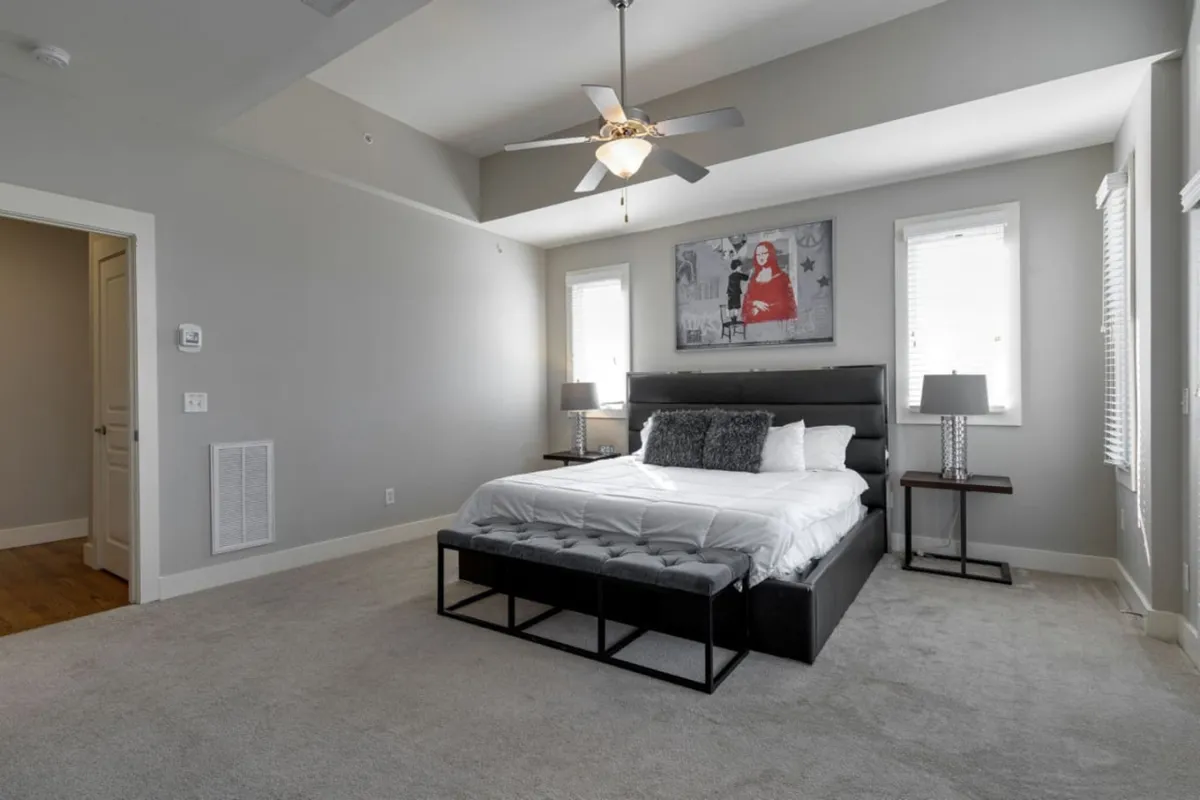 This image showcases a king-sized bed with tasteful artwork above the headboard and matching bedside lamps. Soft natural light filters into the room, creating a tranquil atmosphere ideal for relaxation after a day of exploring Nashville. The room exudes comfort, inviting guests to unwind, read, or simply enjoy peaceful moments together.