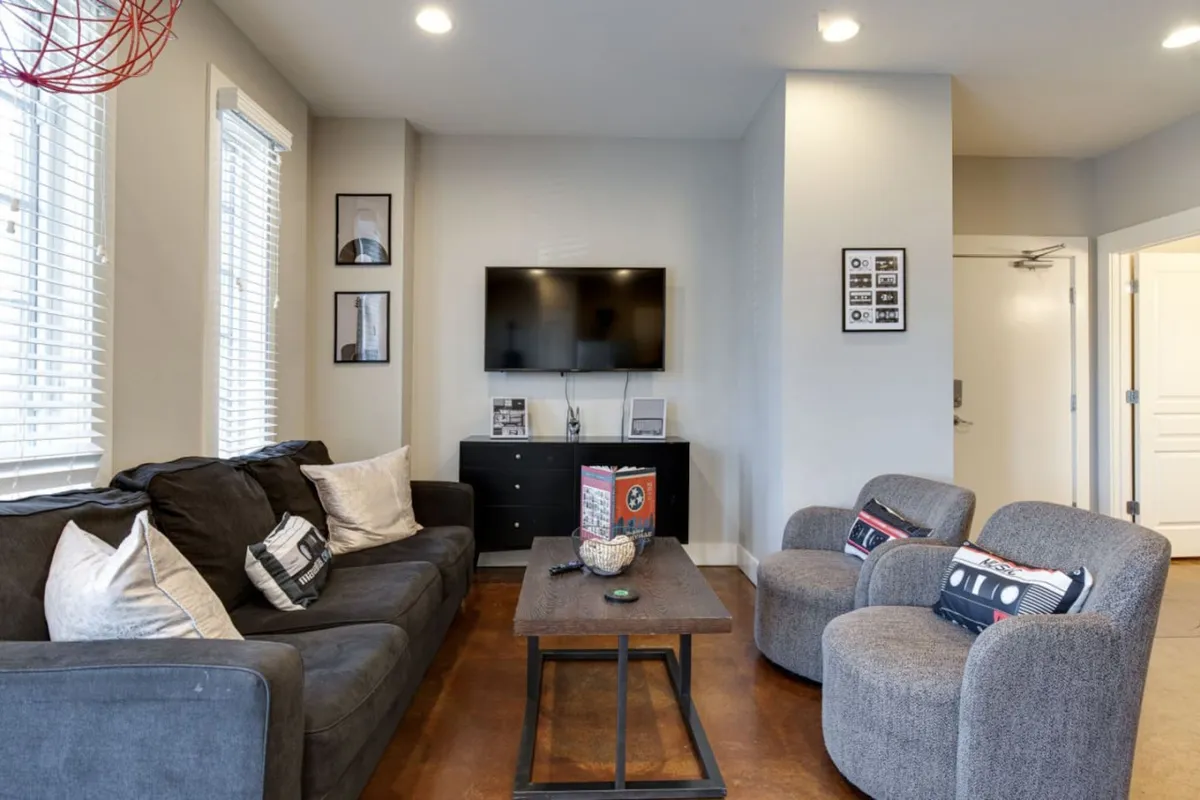 A comfortable living room with a plush sofa, coffee table, TV, and armchairs, accented by decorative items. The room is arranged for both relaxation and conversation, and the overall mood feels welcoming and homey.