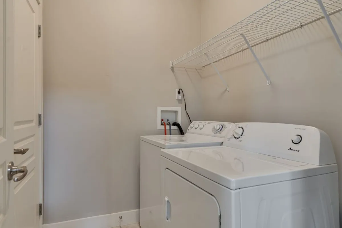 A well-lit laundry area with a washing machine and dryer neatly positioned under a shelf stocked with laundry supplies. The space conveys a sense of cleanliness and efficiency, perfect for managing household tasks with ease.