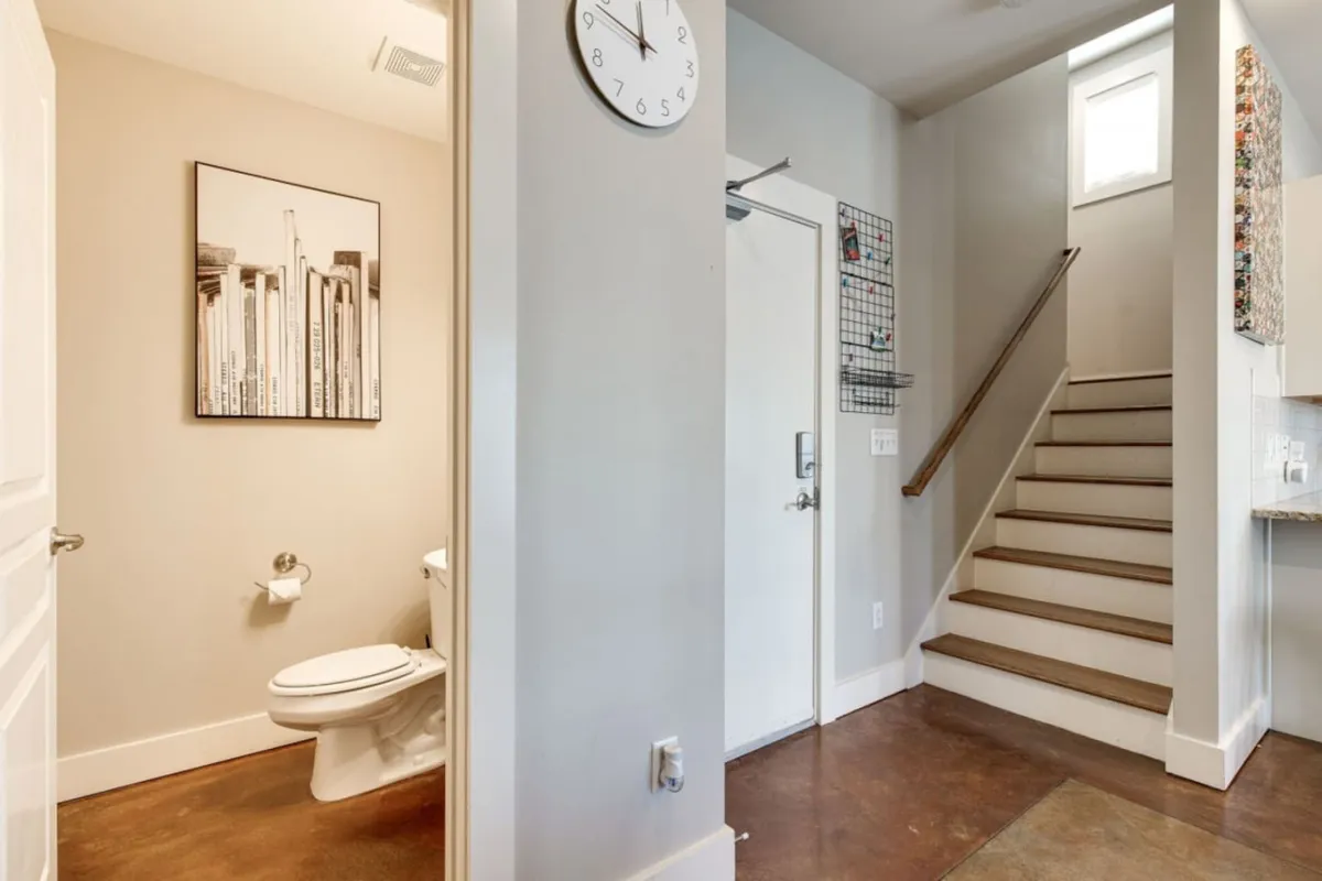 A spacious, organized interior entryway, featuring a clock on the wall, artwork, and a staircase. The area feels calm and welcoming, suggesting an efficient transition space for arrivals and departures.